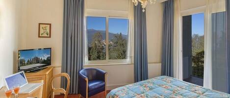 A hotel room with a bed, a desk with a laptop, a chair, a television, and a window with curtains.