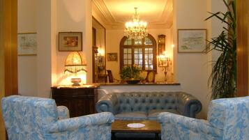 Quarto com um sofá azul estampado, duas poltronas, uma mesa de centro de madeira, um lustre e obras de arte emolduradas nas paredes.