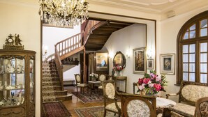 Un vestíbulo imponente con una escalera, muebles ornamentados y un candelabro.