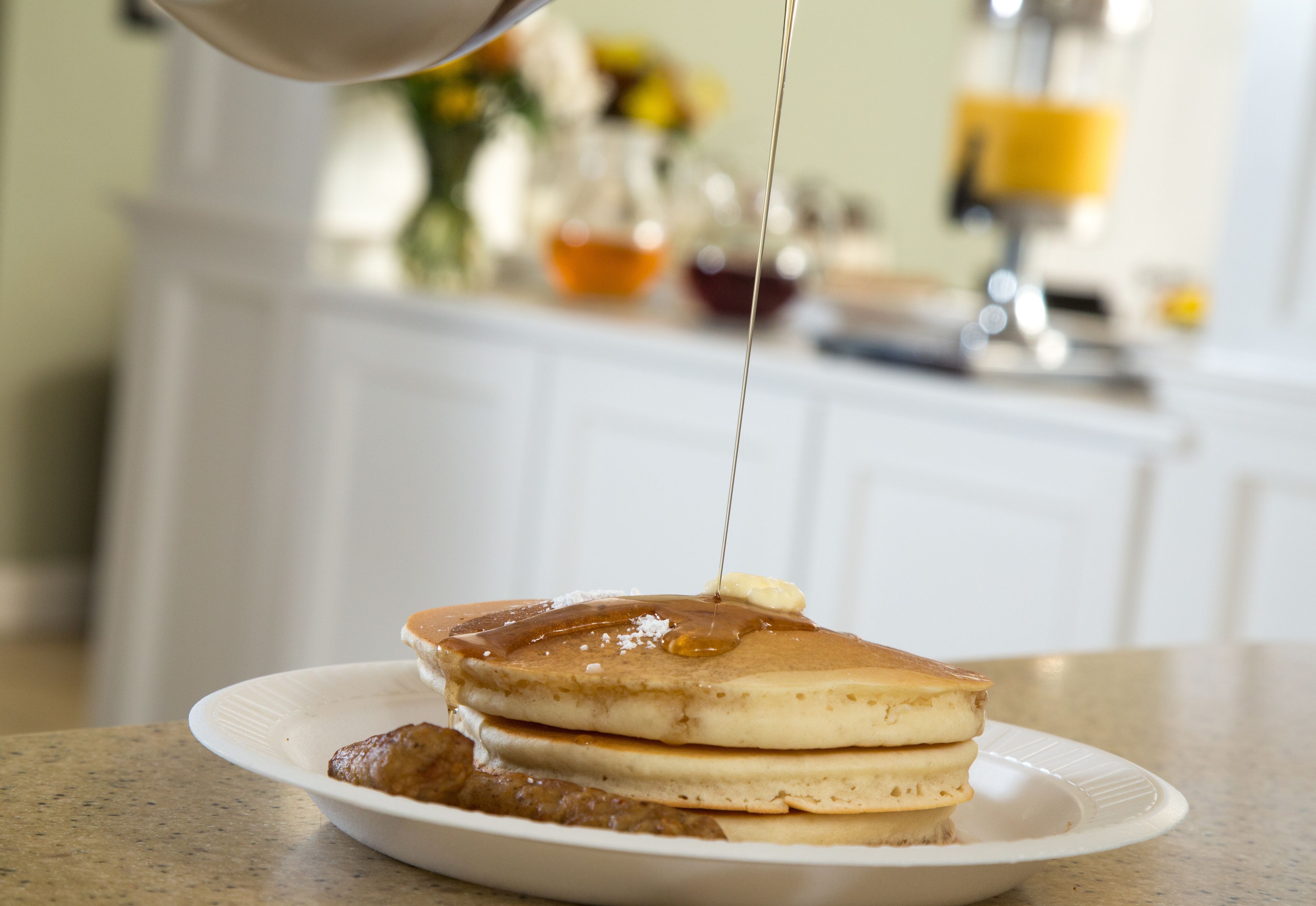 A stack of pancakes with syrup being poured on top.