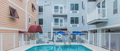 A swimming pool area with a fenced deck, a lifeguard chair, and a sign indicating a no diving zone.