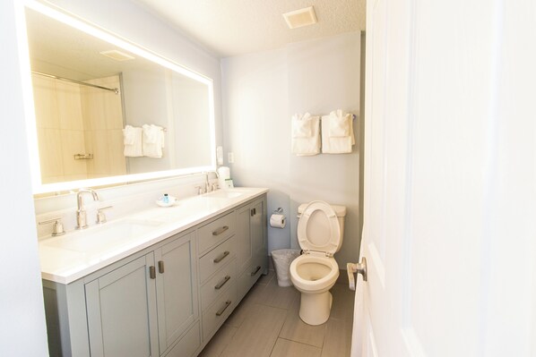 A bathroom with a large mirror, a sink, a toilet, and a trash can.