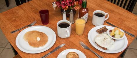 A wooden table with breakfast items including pancakes, eggs, and a muffin. There are salt and pepper shakers, a bottle of ketchup, a cup of coffee, and a glass of orange juice.