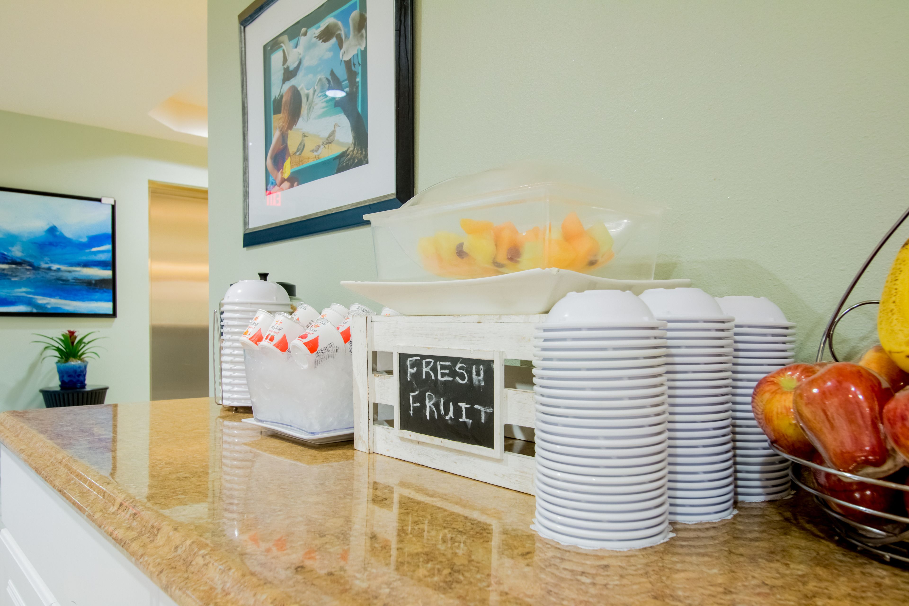 A breakfast area with fresh fruit, stacked plates, and a sign indicating 'FRESH FRUIT'.
