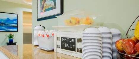 A breakfast area with fresh fruit, stacked plates, and a sign indicating 'FRESH FRUIT'.