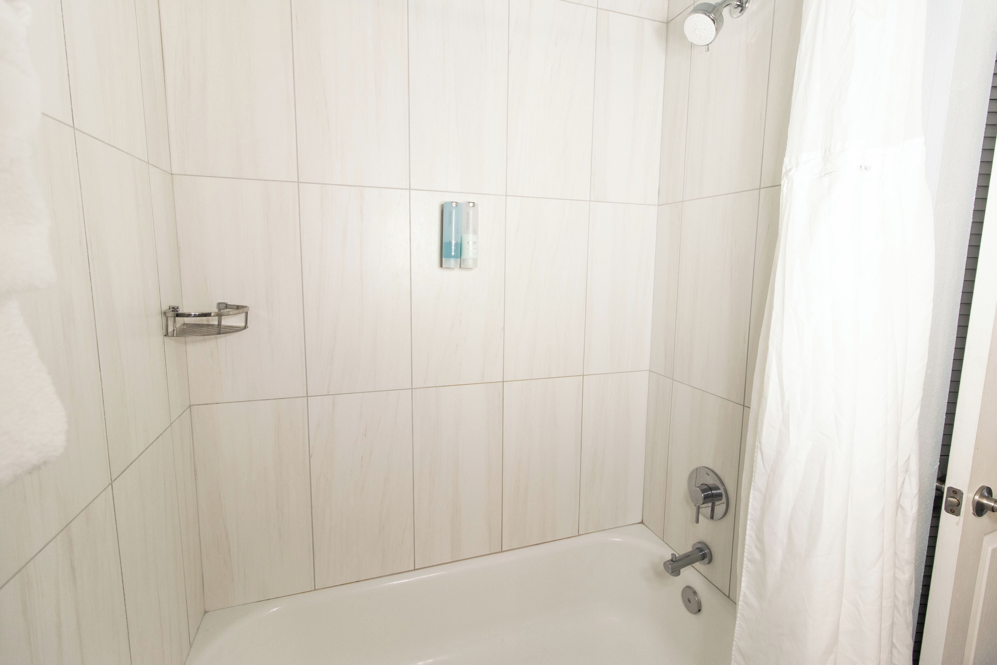 A bathroom with white tiles, a bathtub, a shower, and a towel rack.