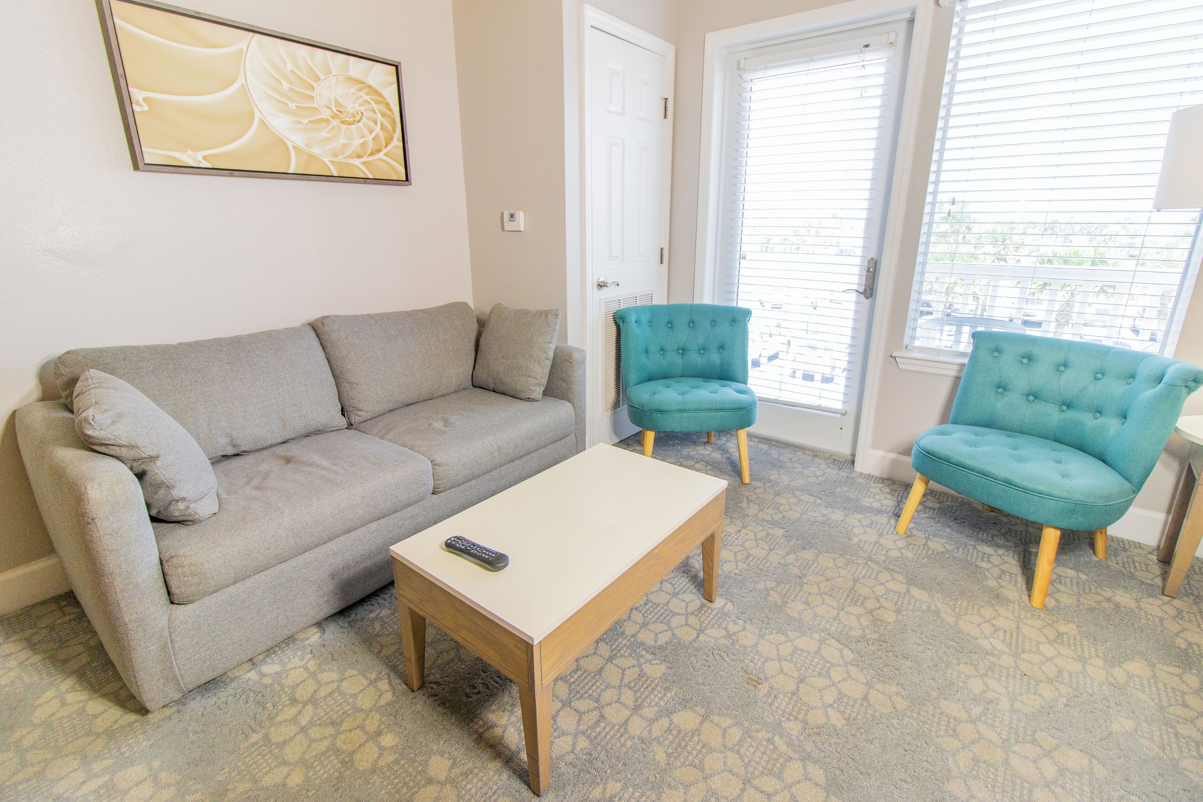 A living room with a grey sofa, two teal armchairs, a wooden coffee table, and a patterned carpet.