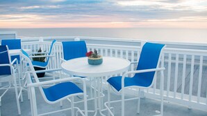 A terrace with white railings, blue chairs, and a white table with a potted plant.