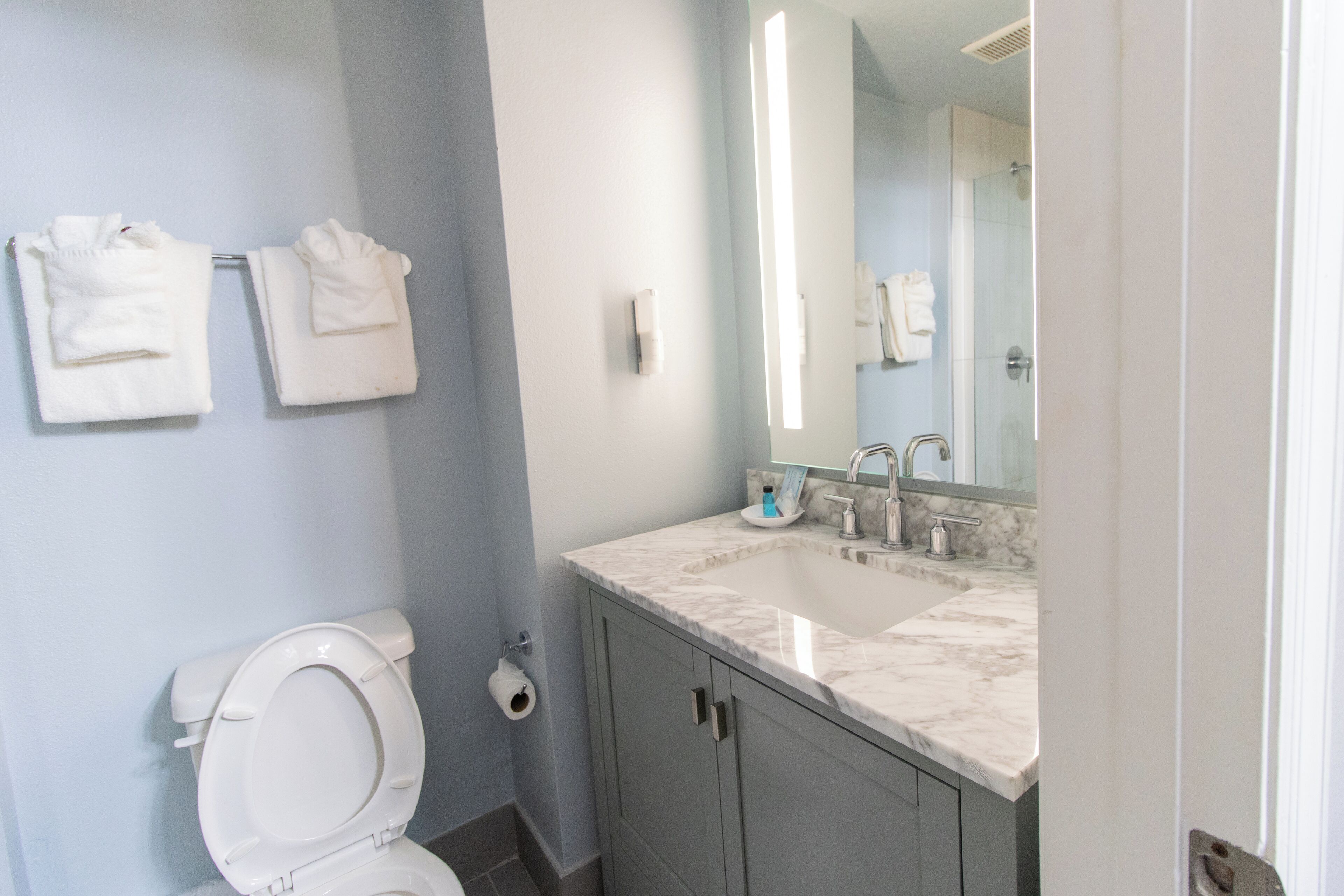 A bathroom with a toilet, a sink with a mirror, and two towels hanging on the wall.