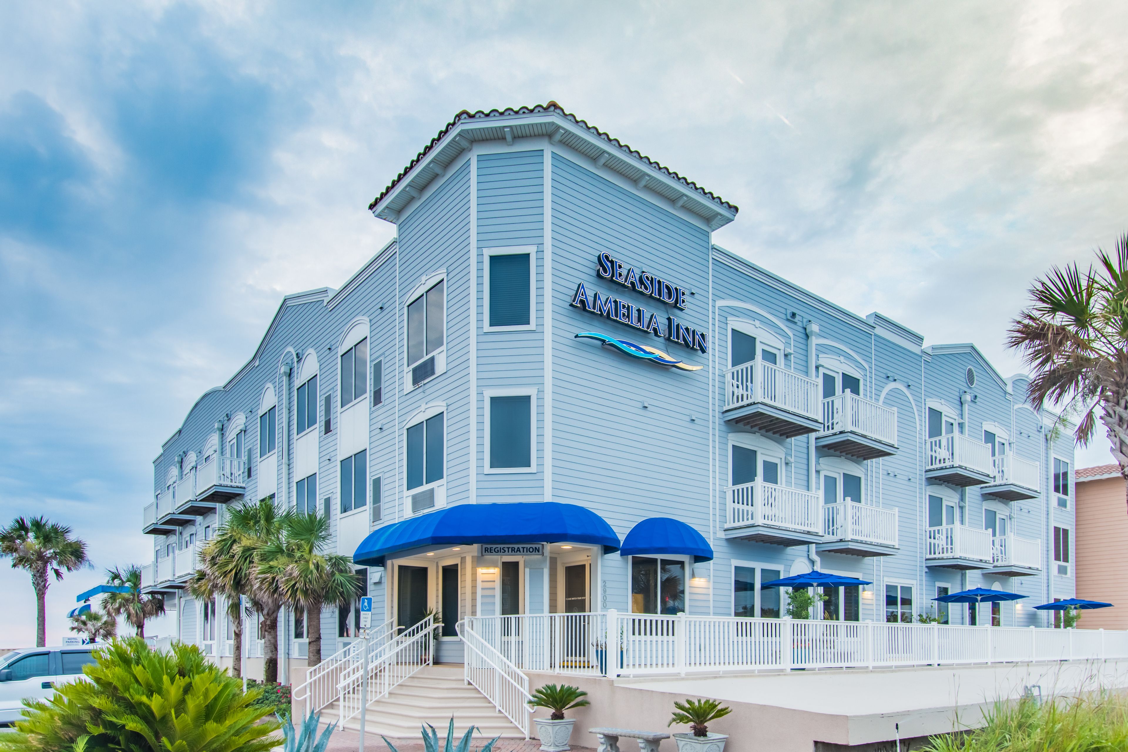 A Seaside Amelia Inn with a registration area, outdoor seating with blue umbrellas, and a balcony on the second floor.