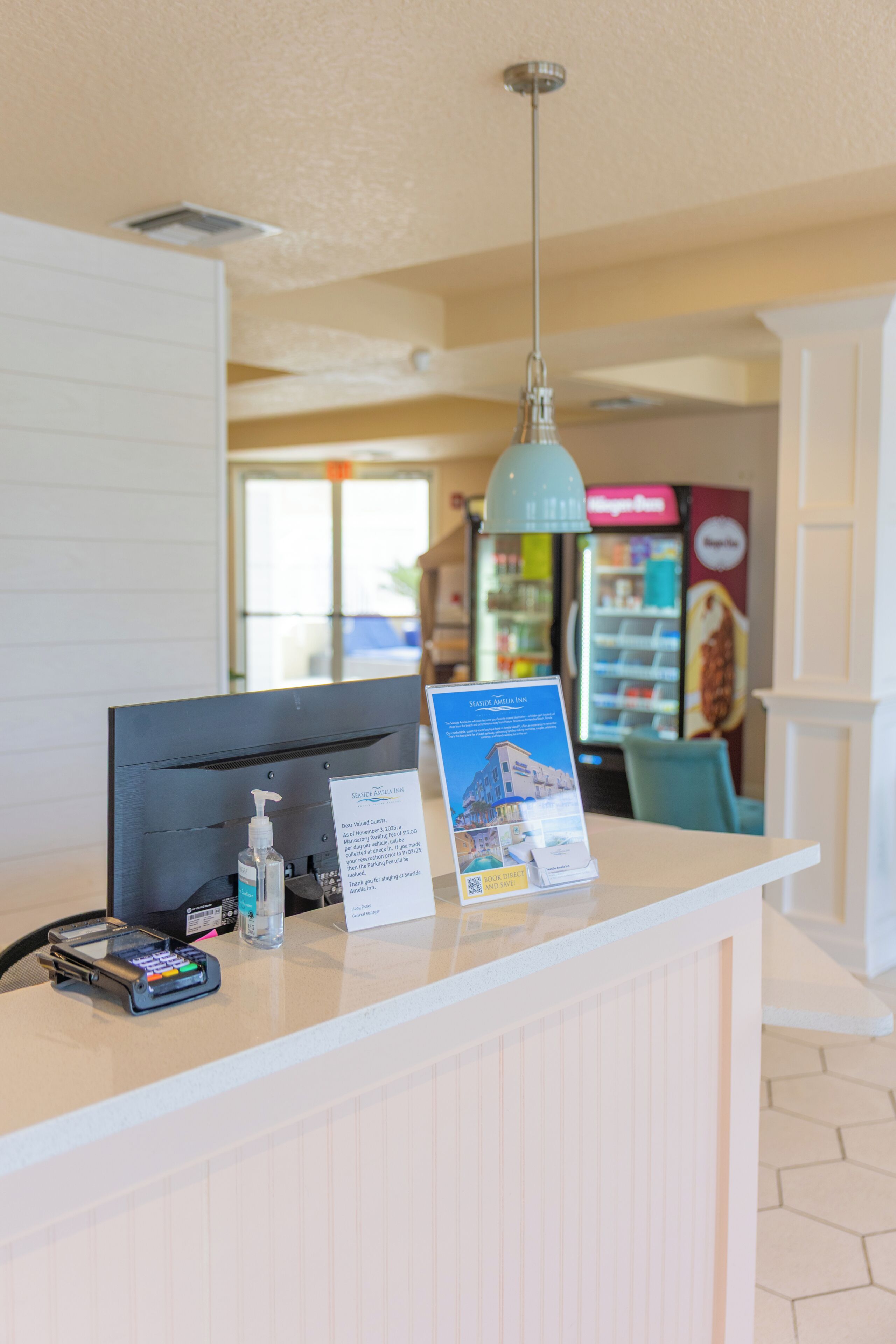 A reception desk with a digital kiosk, a bottle of hand sanitizer, and a sign with a building illustration.