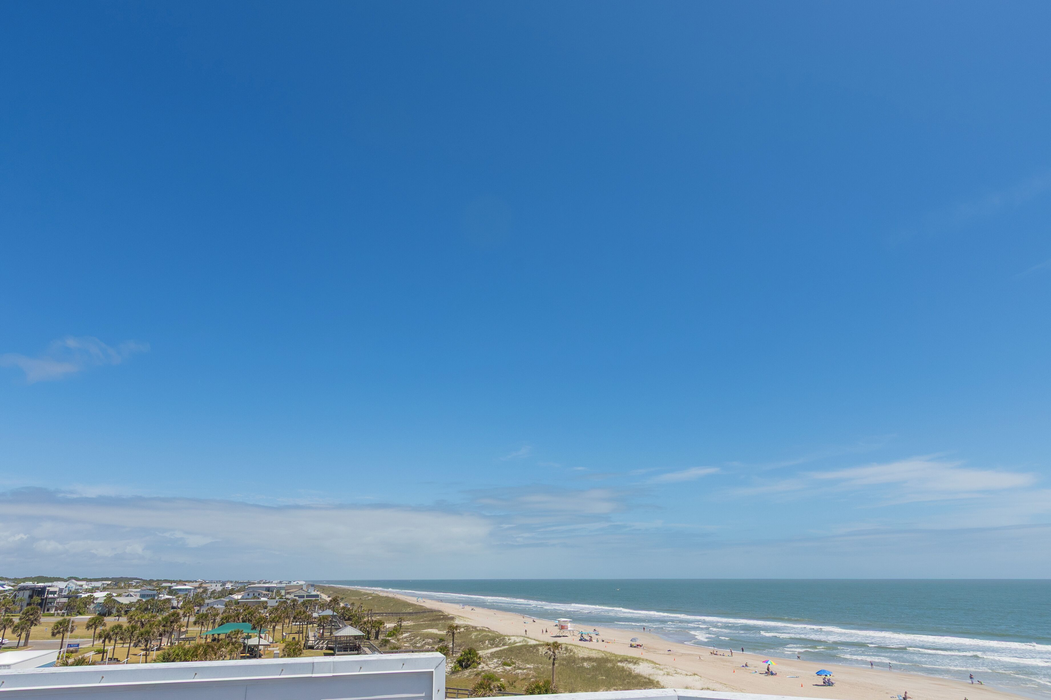 A beach view with a clear sky, a sandy shore, and a few umbrellas.