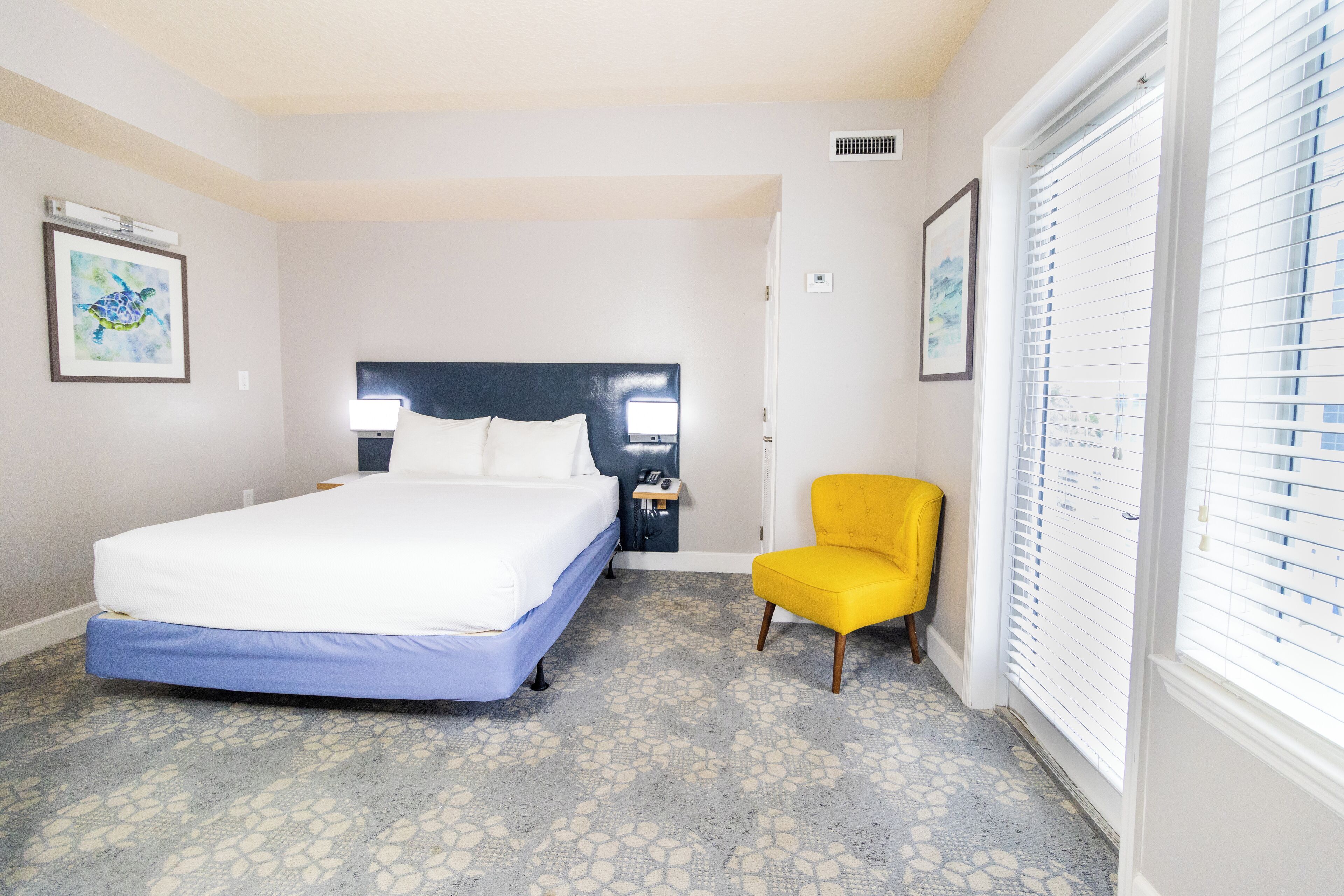 Une chambre à coucher comprenant un lit, une table de chevet, une chaise et une fenêtre avec des stores.