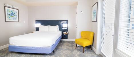 A bedroom with a bed, a nightstand, a chair, and a window with blinds.