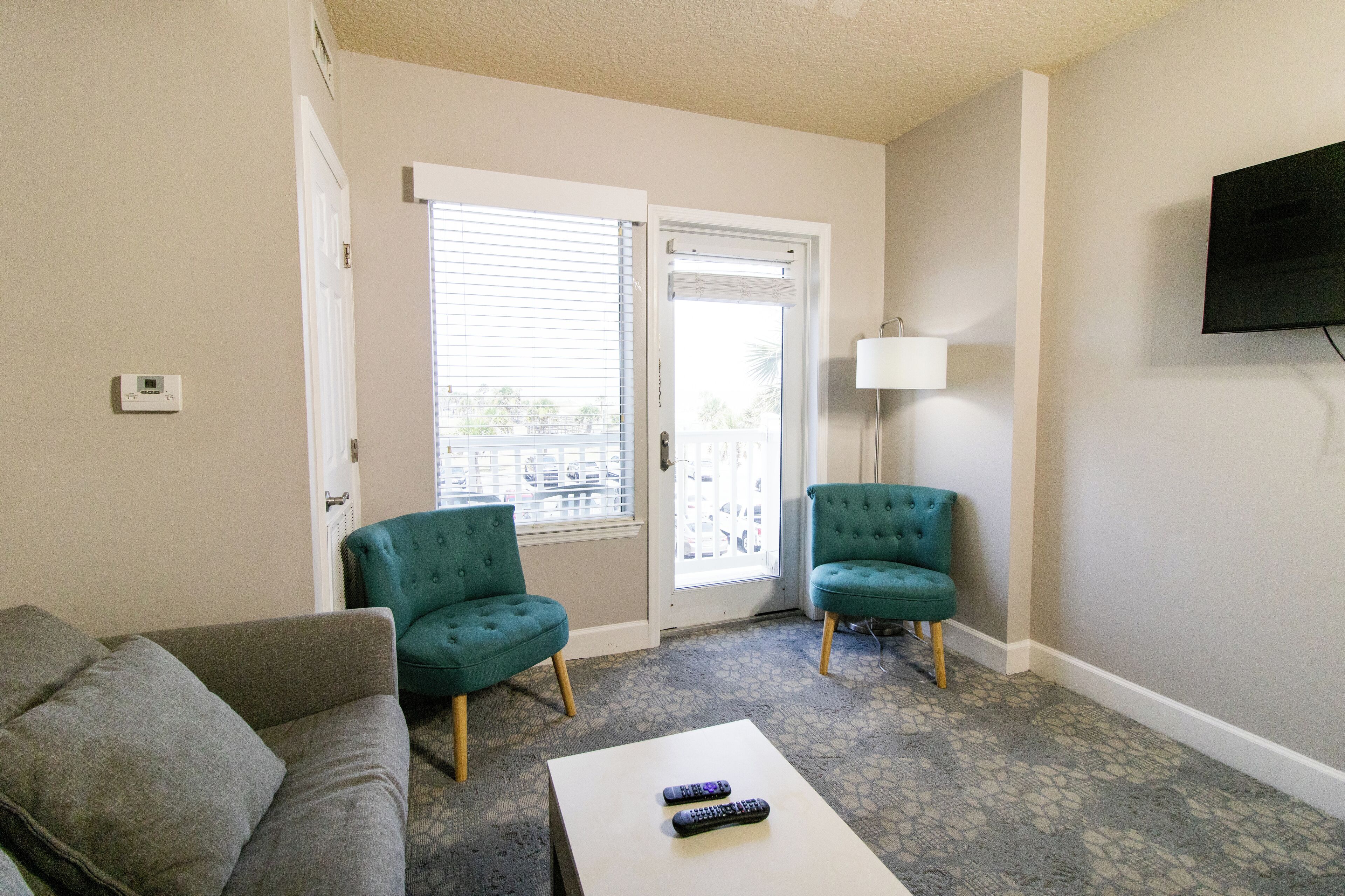 A living room with two teal armchairs, a grey sofa, and a coffee table with two remotes.