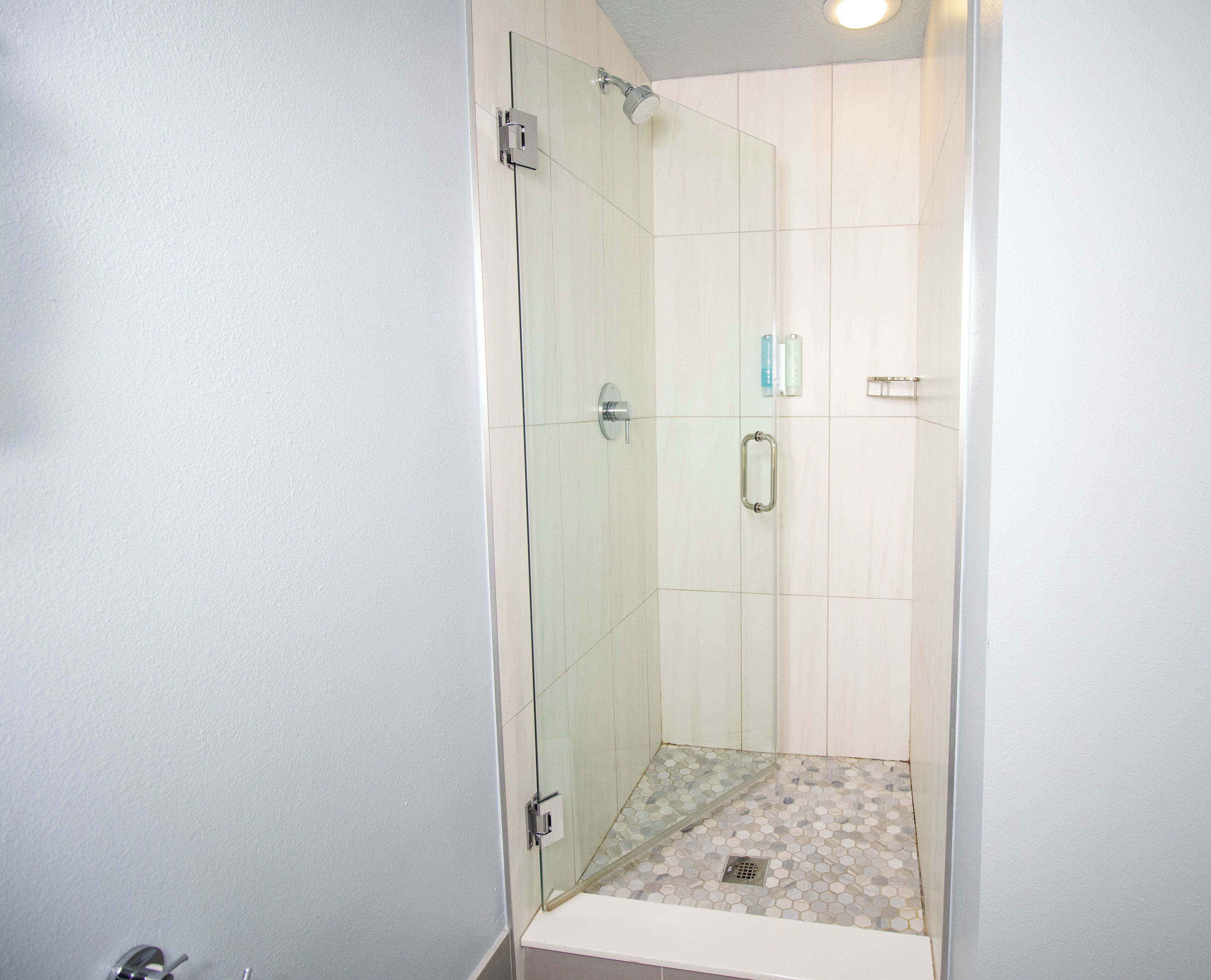 Ducha con paredes de vidrio, suelo de baldosas y pared blanca.