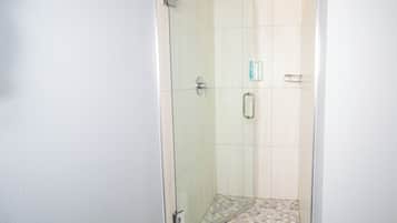 Une douche fermée par des parois de verre, avec un sol carrelé et un mur blanc.