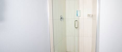 Ducha con paredes de vidrio, suelo de baldosas y pared blanca.