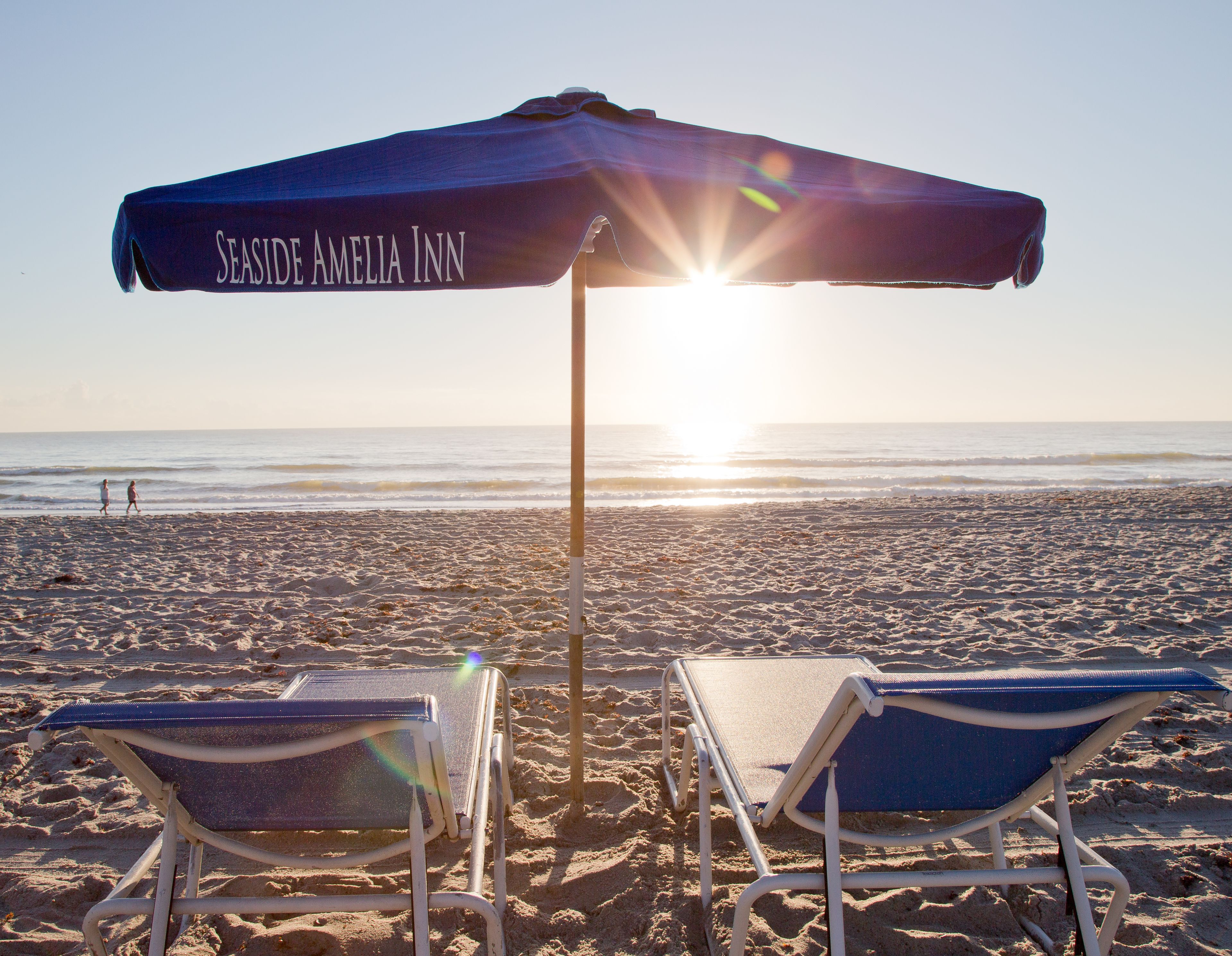 Une plage avec deux chaises longues et un auvent portant l’inscription « Seaside Amelia Inn ».