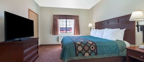 Habitación de hotel con cama, televisor en una cómoda, ventana con cortinas y mesita de noche con lámpara.