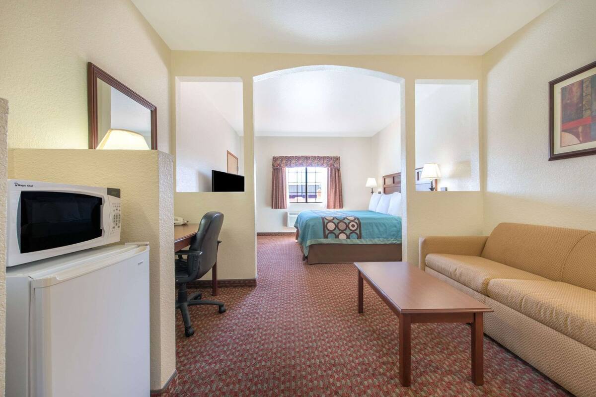 A hotel room with a microwave, a desk, a chair, a bed with a patterned bedspread, a sofa, and a small table.