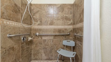 A shower area with a handrail, a grab bar, and a shower chair.