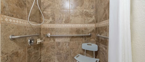 A shower area with a handrail, a grab bar, and a shower chair.