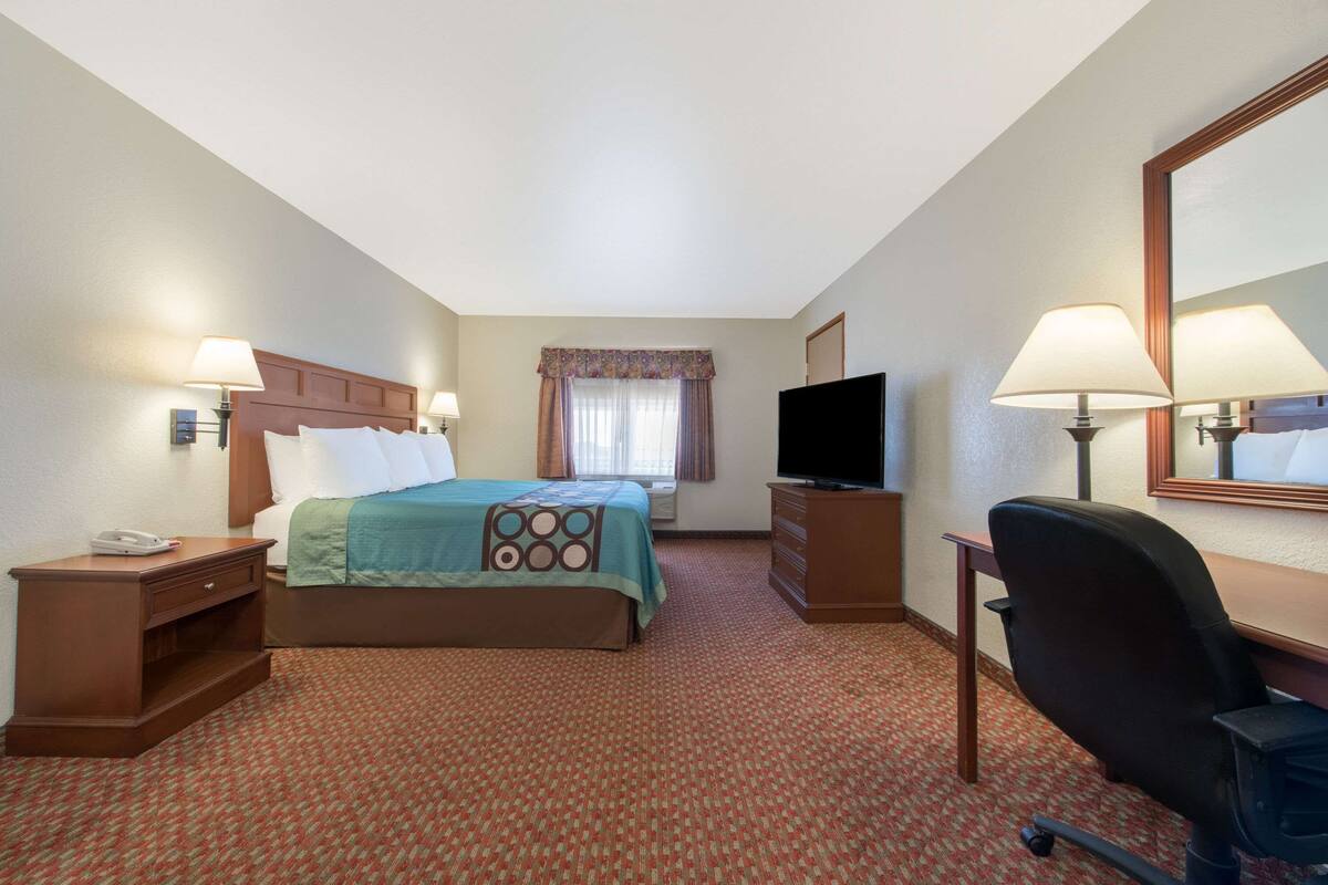 A hotel room with a bed, a desk, a chair, a TV, and a window with curtains.