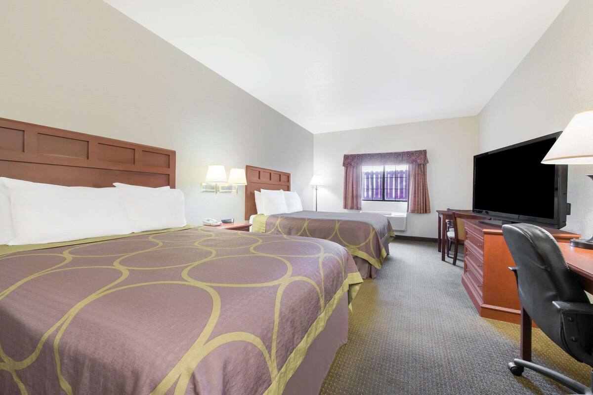 A hotel room with two beds, a desk, a chair, a television, and a window with curtains.