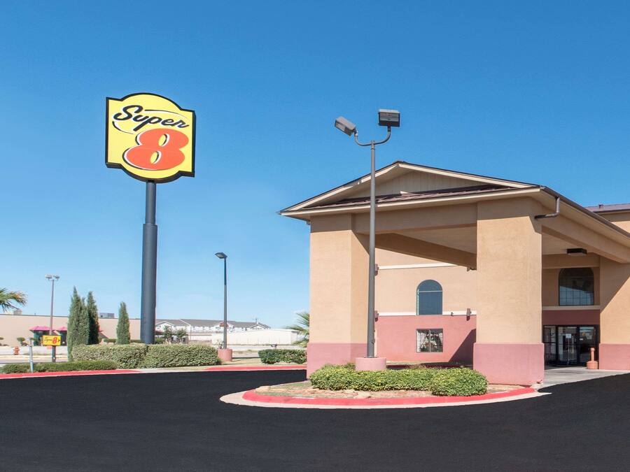 Un hotel con un llamativo letrero de 'Super 8', un acceso cubierto y un estacionamiento con bordes rojos.