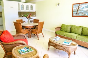 Un salon avec des meubles en osier, un canapé vert et un coin repas comprenant une table et des chaises.