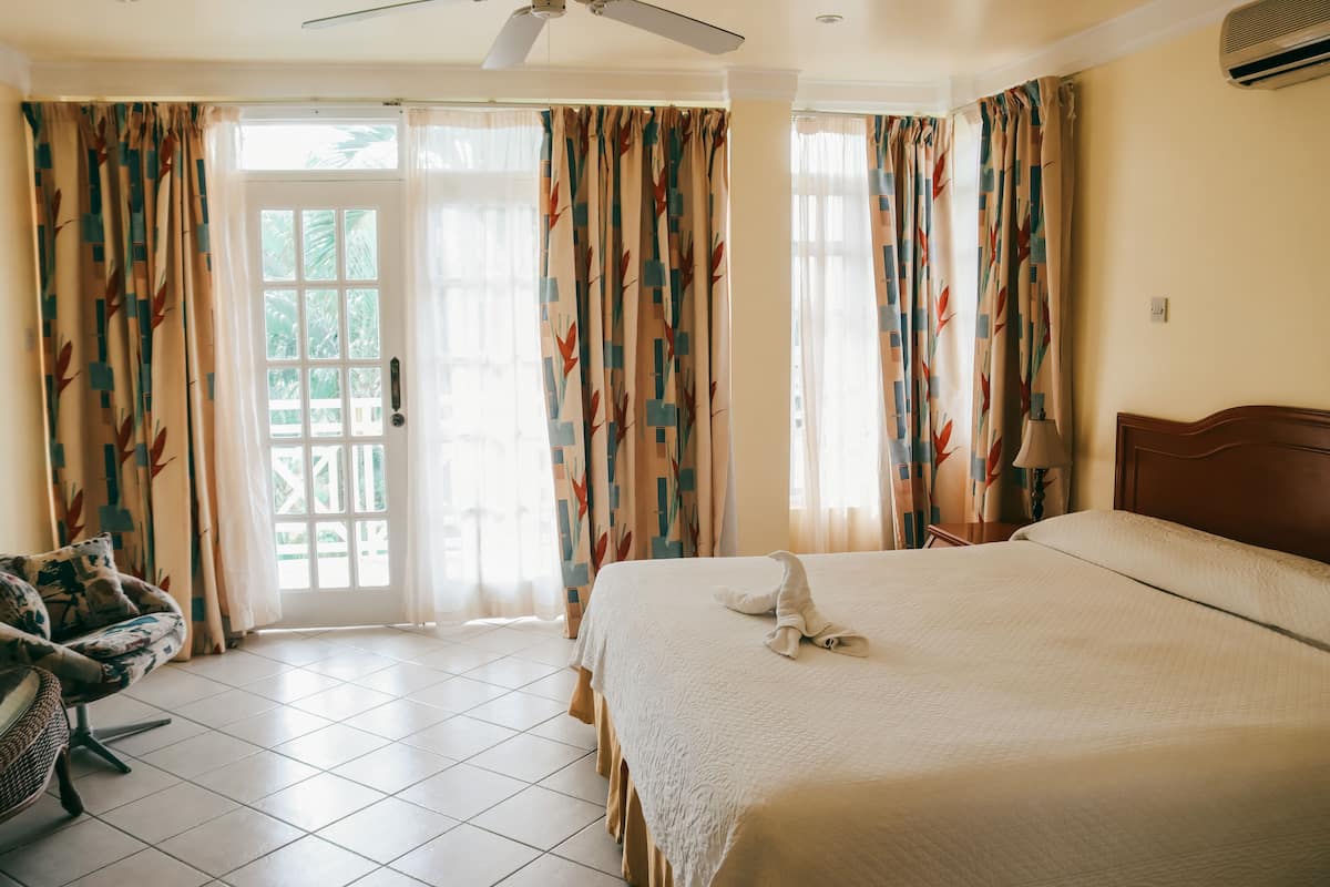 A hotel room with a bed, curtains, a chair, and a ceiling fan.