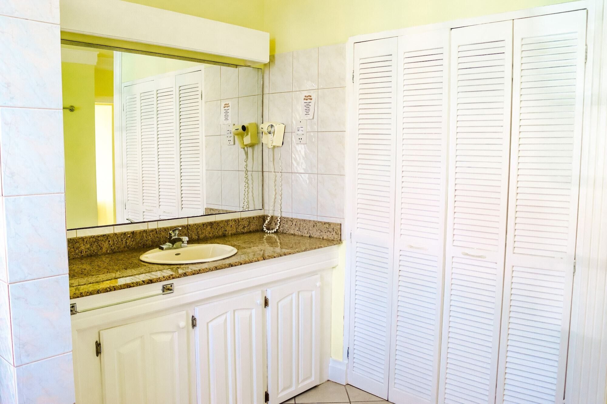 Un baño con lavamanos, espejo y armarios blancos.
