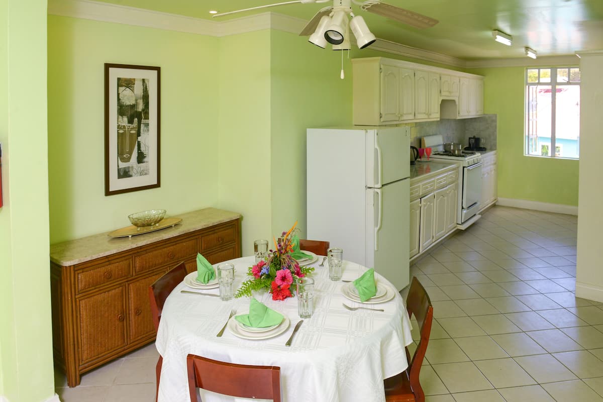 A dining area with a table set for four, a refrigerator, and a kitchen in the background.