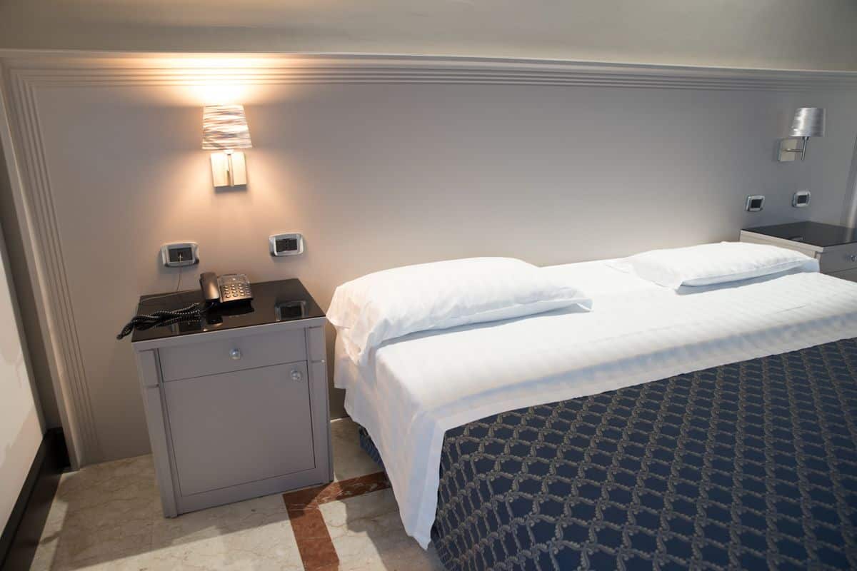 Una habitación de hotel con cama, escritorio y teléfono, y una lámpara de pared.