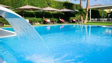 Une piscine avec un toboggan, des chaises longues, des parasols et une pelouse bien entretenue.
