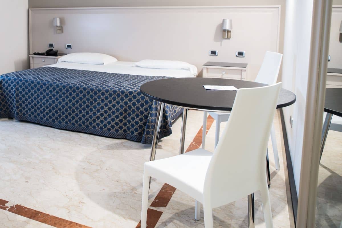 Una habitación de hotel con cama, mesitas de noche, escritorio, silla y una pequeña mesa con otra silla.