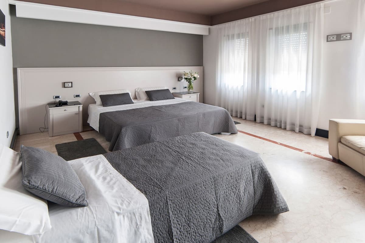 Una habitación de hotel con dos camas, un escritorio, una silla y un ventanal con cortinas.