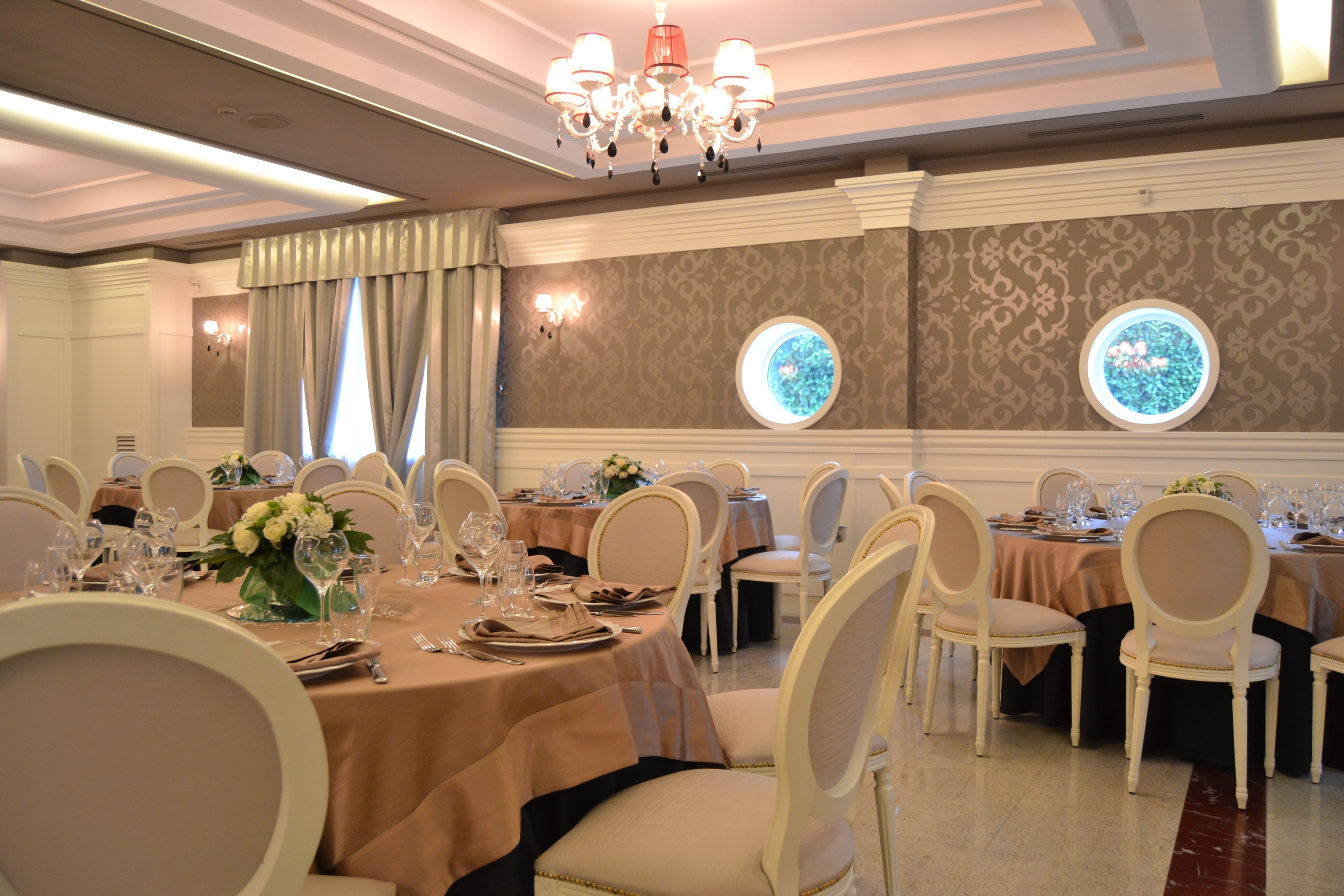 A banquet hall with round tables, white chairs, and chandeliers.