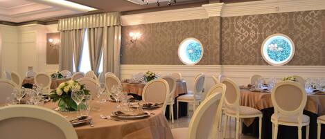 A banquet hall with round tables, white chairs, and chandeliers.