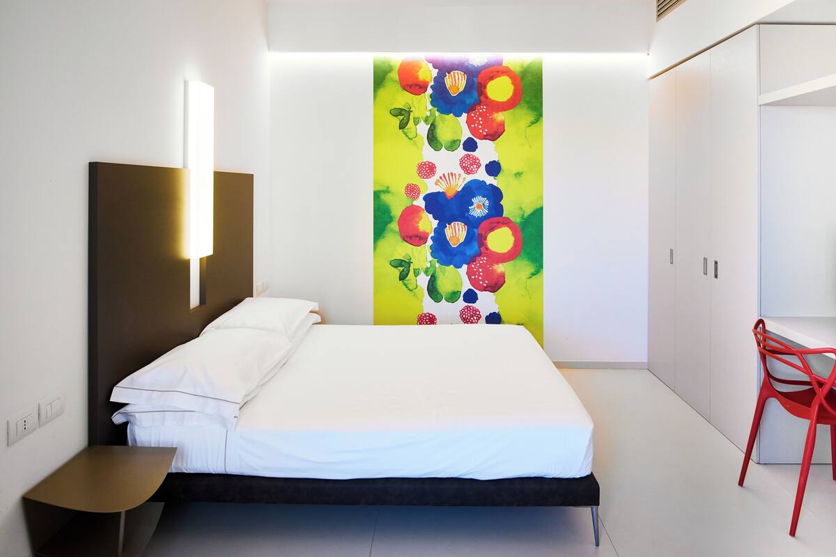 A modern bedroom with a bed, bedside table, and a colorful abstract painting on the wall.
