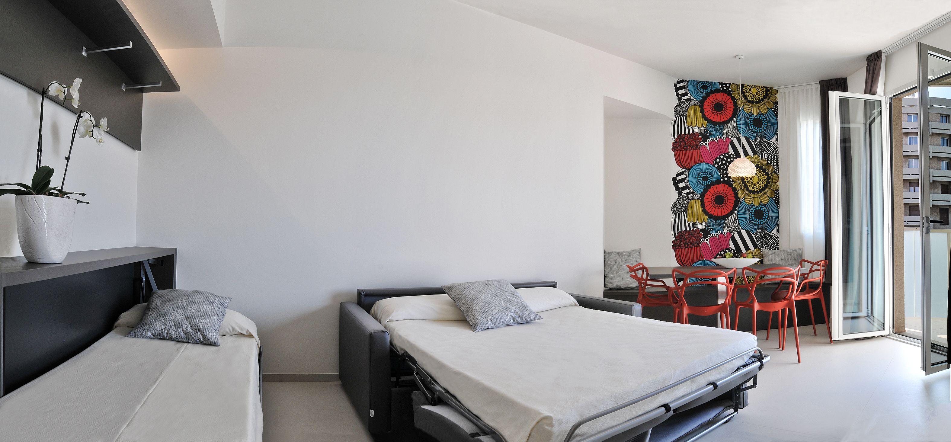 Un dormitorio moderno con una cama, un escritorio y una silla. Hay una obra de arte colorida en la pared y una planta en maceta.