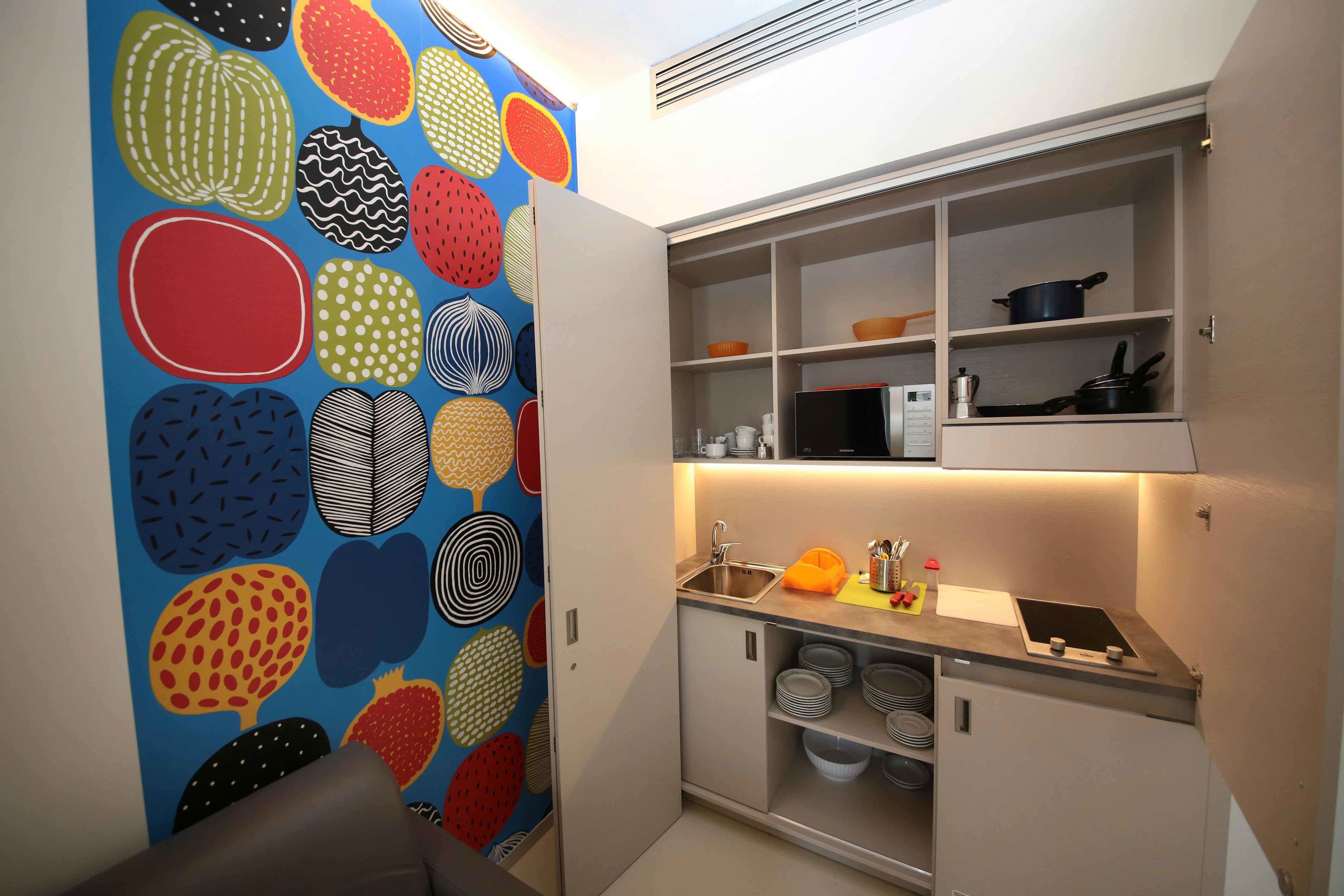 A compact kitchen with a built-in oven, a sink, and a countertop with a kettle and a small stove.