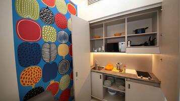 A compact kitchen with a built-in oven, a sink, and a countertop with a kettle and a small stove.