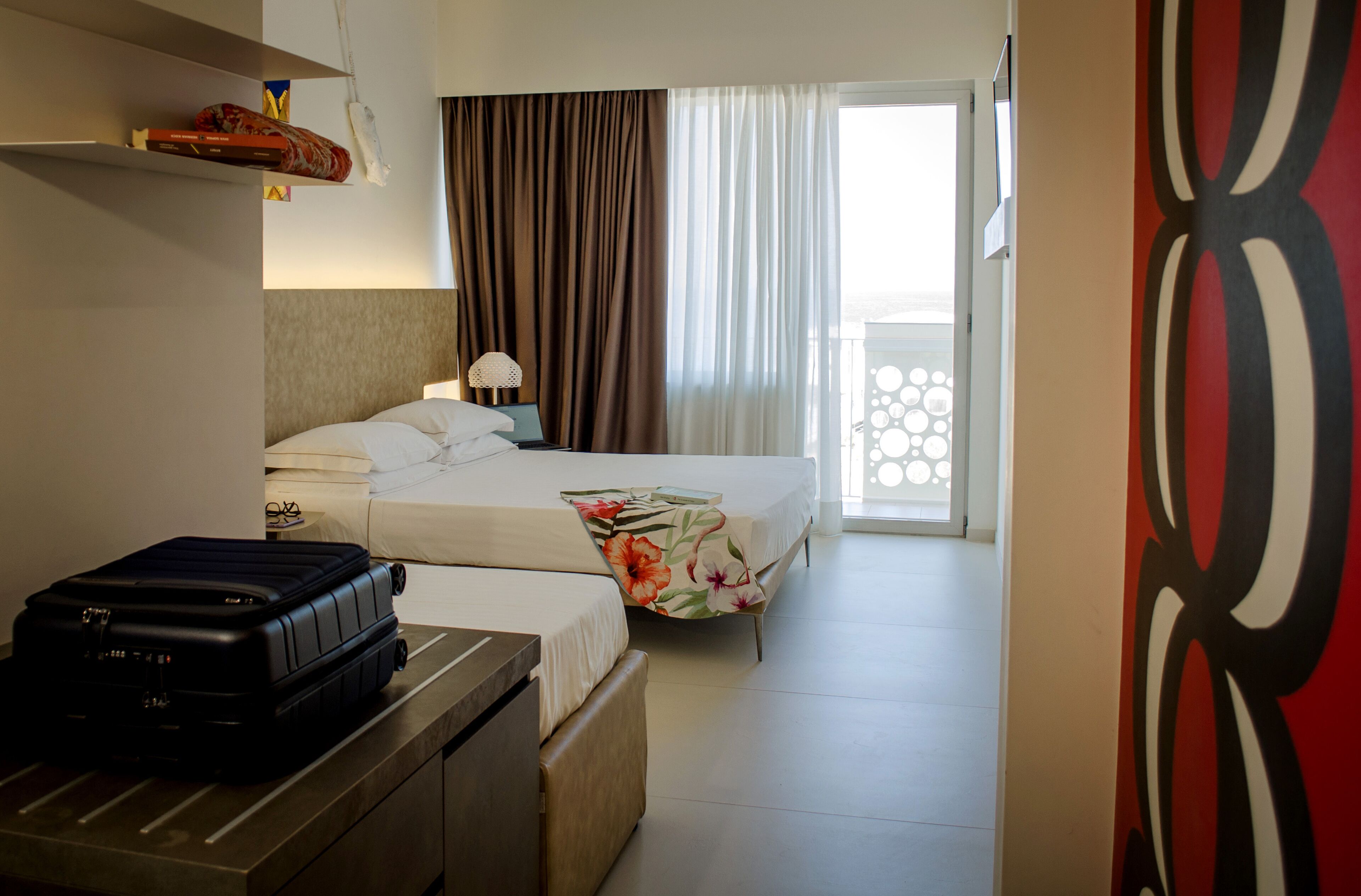 Een hotelkamer met een bed, een koffer, een nachtkastje en uitzicht op het balkon.