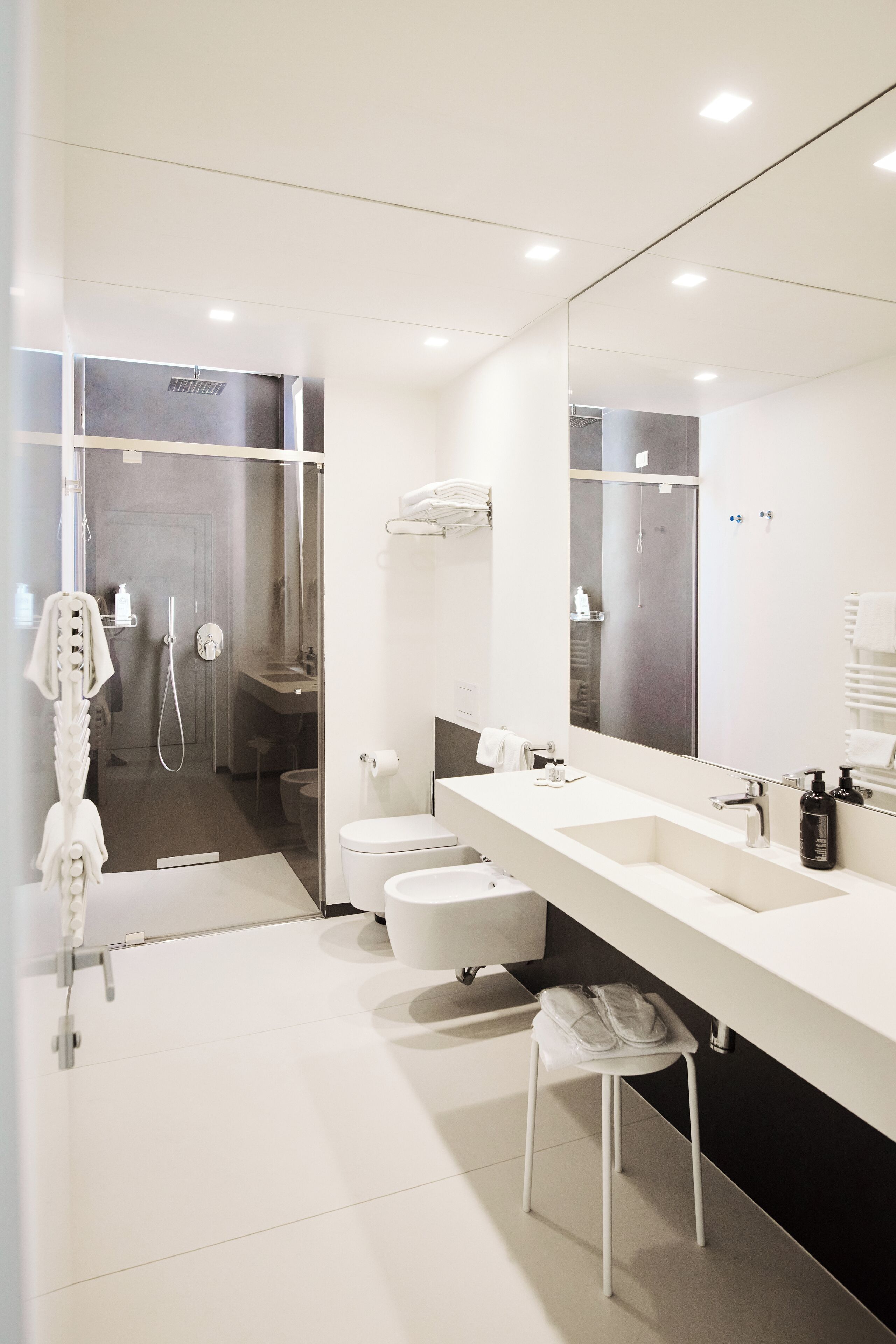 Une salle de bain moderne avec un grand miroir, deux lavabos, des toilettes et un espace douche.