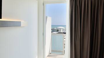 A hotel room with a bed, a TV mounted on the wall, and a view of the sea through a balcony door.