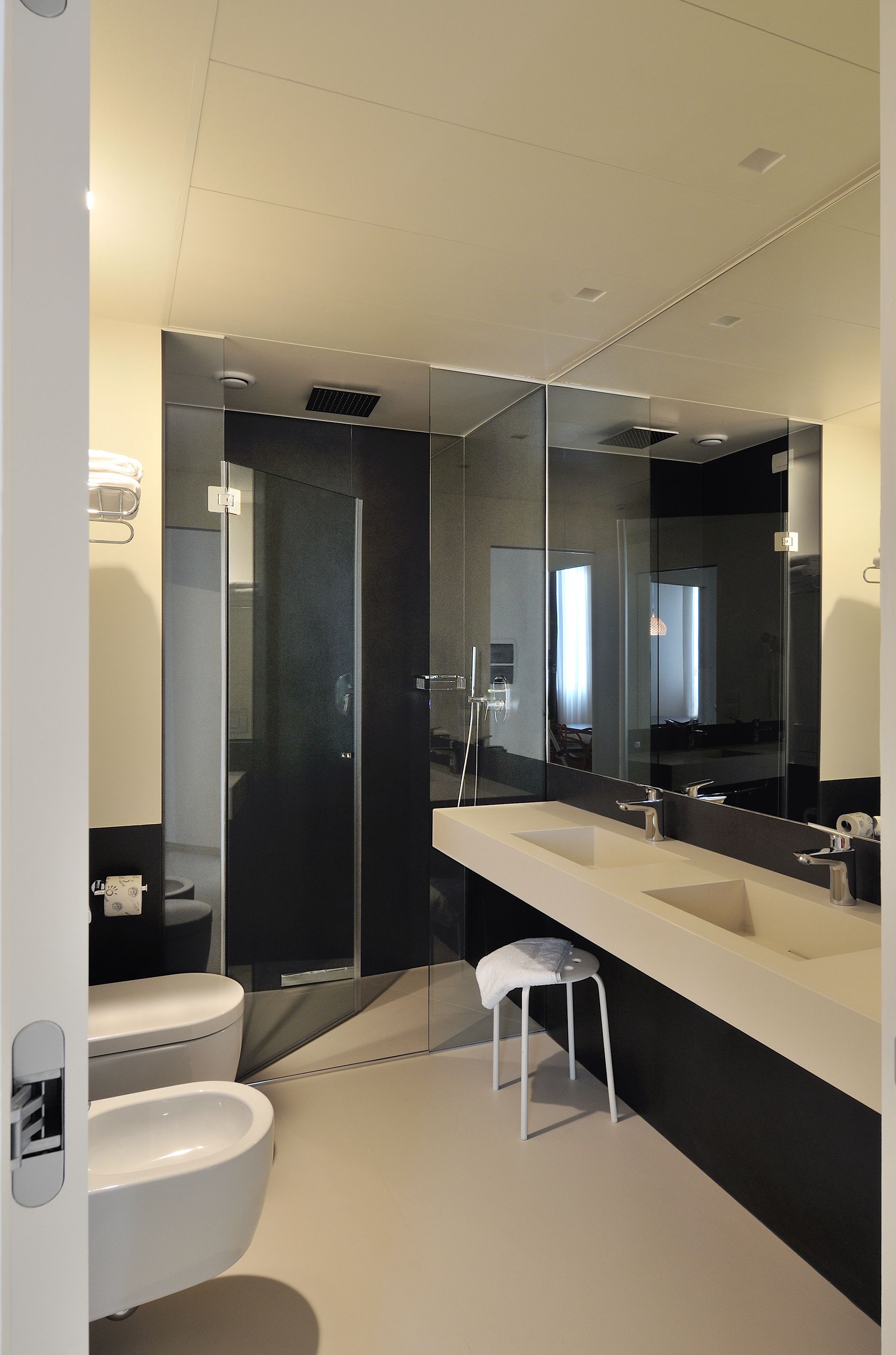 Un baño moderno con un espejo grande, dos lavamanos, un inodoro y un box de ducha.