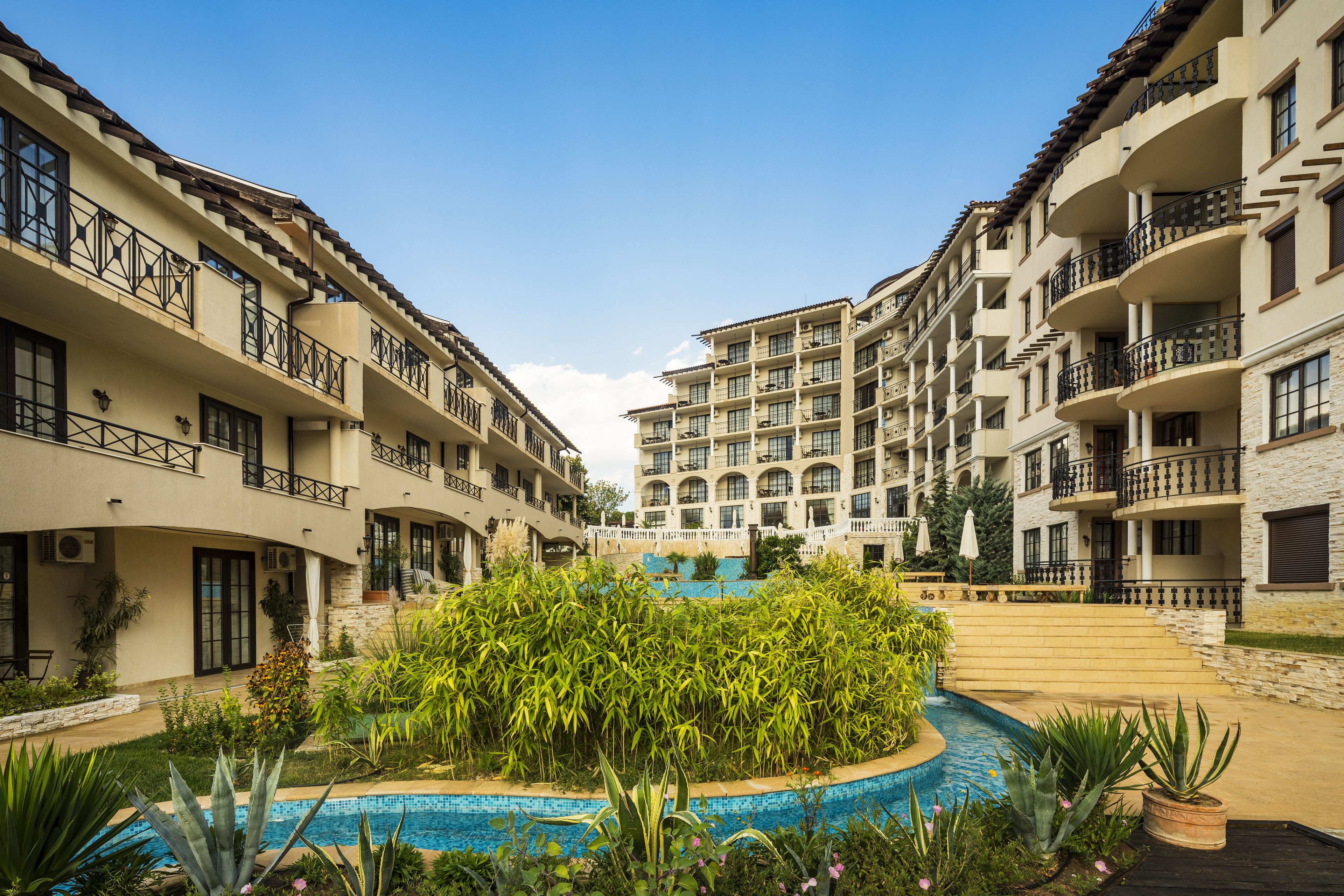 Un patio de hotel con piscina rodeado de exuberante vegetación y edificios de varios pisos con balcones.