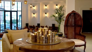 A cozy lounge area with a round wooden table surrounded by cushioned chairs, a sofa, and a large potted plant. - The Cliff Beach & SPA Hotel (Obzor)